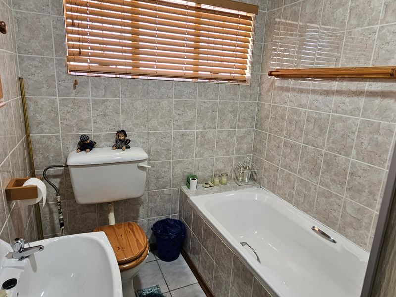 A functional bathroom featuring a bathtub, pedestal basin, and toilet with neutral wall tiling and wooden blinds.