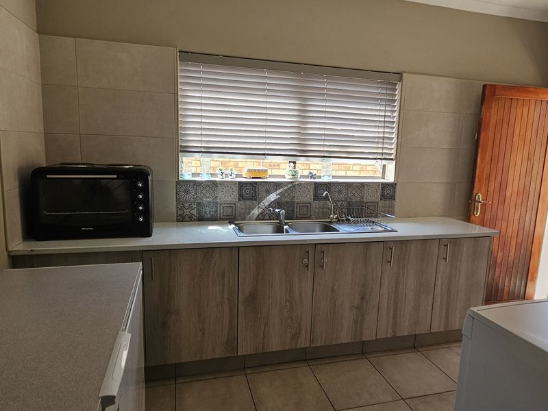 Functional laundry room featuring built-in cabinetry, double sink, tiled splashback, and direct access to the exterior.
