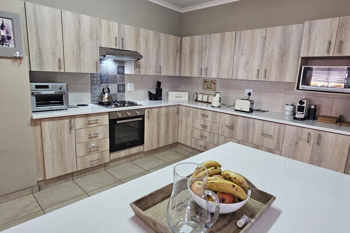 A functional kitchen featuring light wood-grain cabinetry, stone-look countertops, a built-in oven with gas hob, and a dedicated built-in microwave nook.