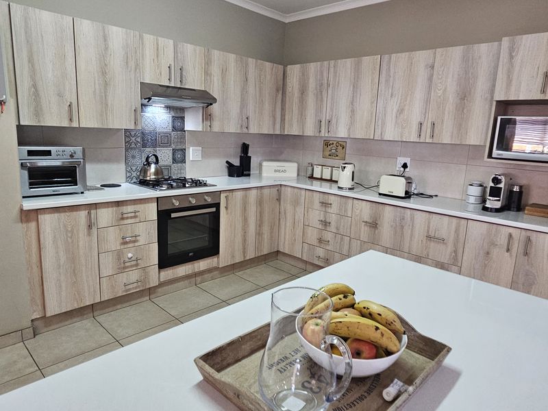 A functional kitchen featuring light wood-grain cabinetry, stone-look countertops, a built-in oven with gas hob, and a dedicated built-in microwave nook.