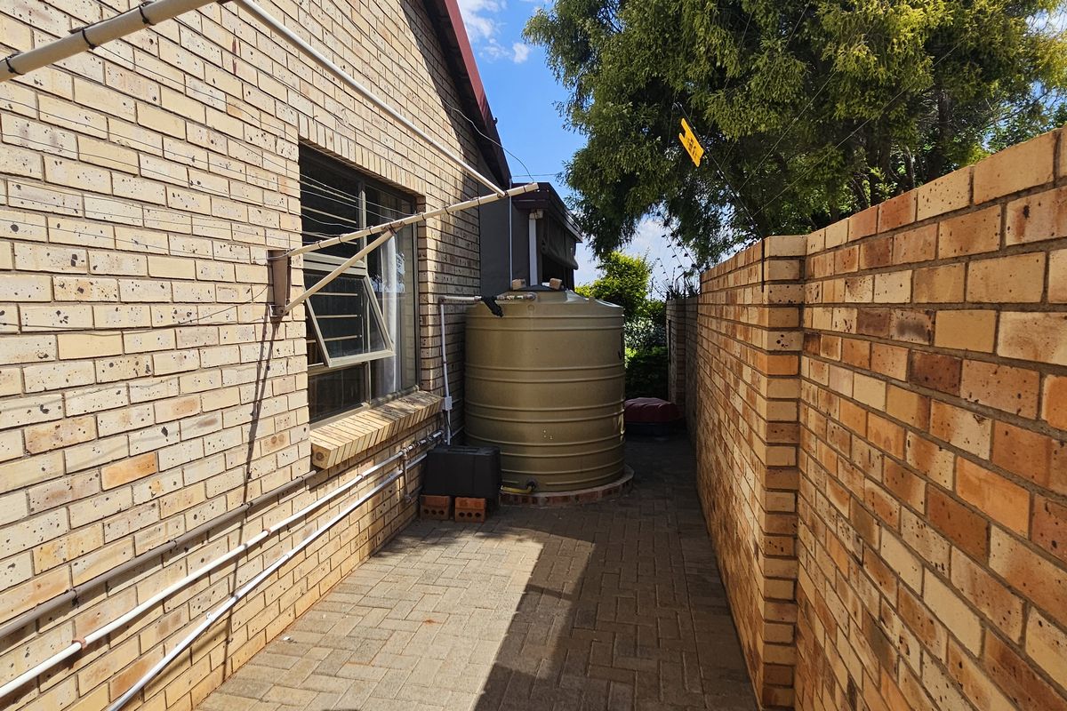 A side exterior walkway featuring brick walls, a paved path, and a large water storage tank.