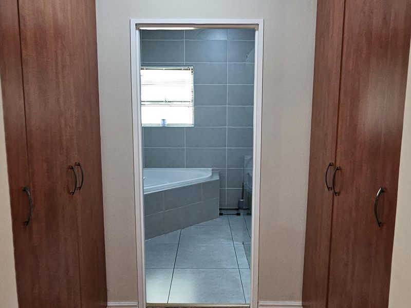 A hallway featuring built-in wooden cupboards leading into a tiled bathroom with a corner bathtub.