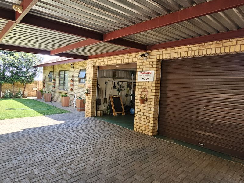 A well-maintained garage with a roller shutter door, featuring an attached carport and paved driveway area.