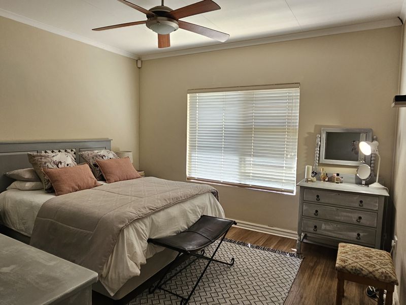 A well-maintained bedroom featuring laminate flooring, a ceiling fan, and venetian blinds, providing a comfortable and functional living space.