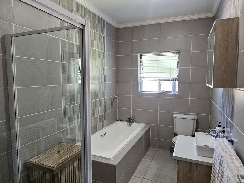 Modern bathroom featuring a tiled shower enclosure, built-in bathtub, vanity with basin, and wall-mounted storage cabinet.