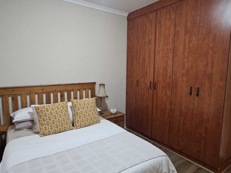 A well-maintained bedroom featuring a large, full-height built-in wooden wardrobe and neutral wall finishes.
