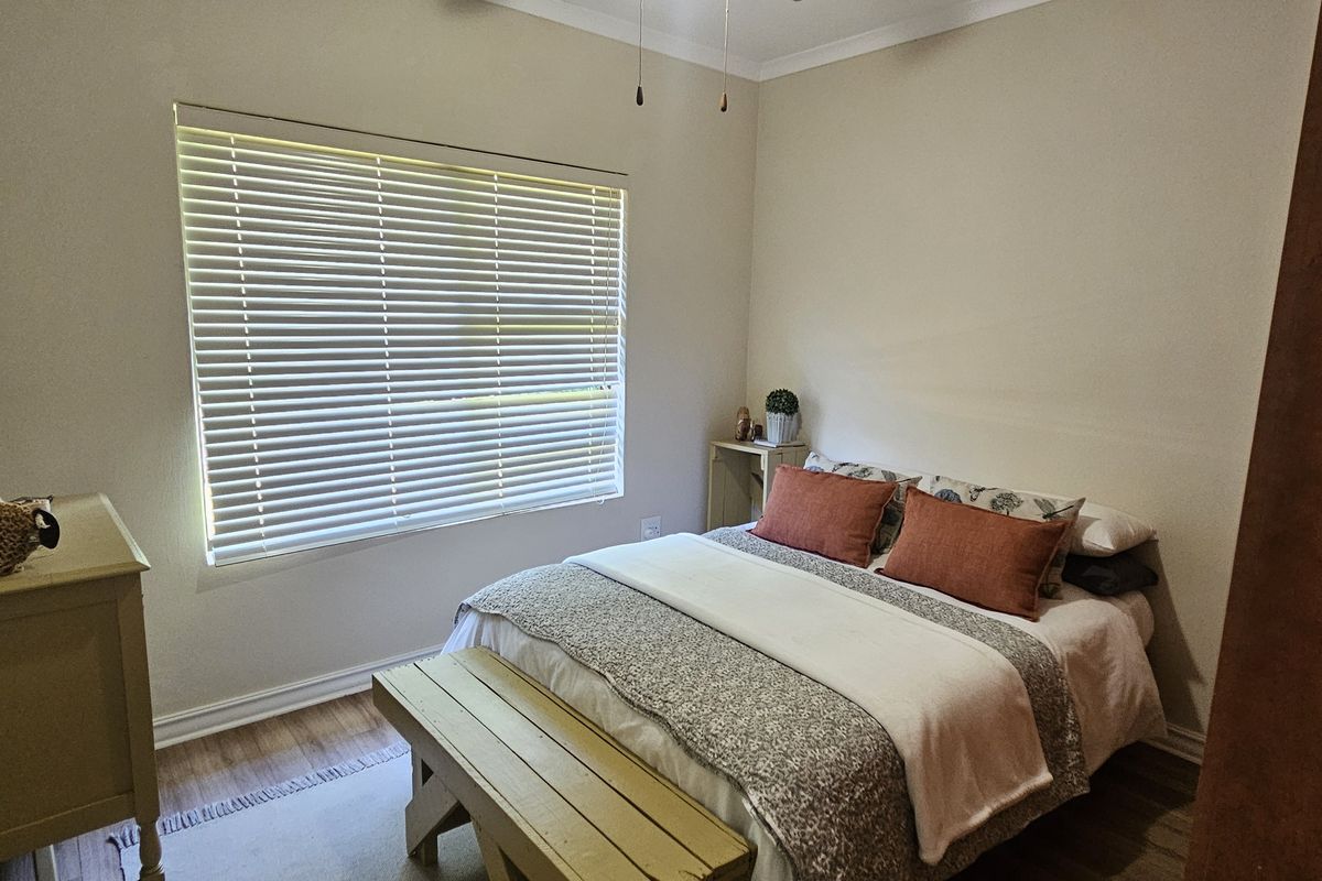 A functional bedroom featuring neutral walls, wood-look flooring, and venetian blinds, providing a comfortable and well-lit space.