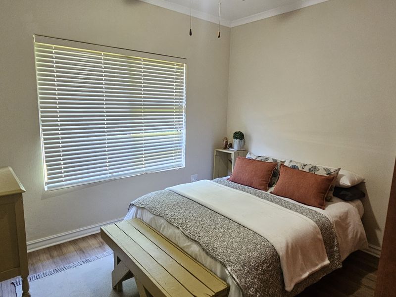 A functional bedroom featuring neutral walls, wood-look flooring, and venetian blinds, providing a comfortable and well-lit space.