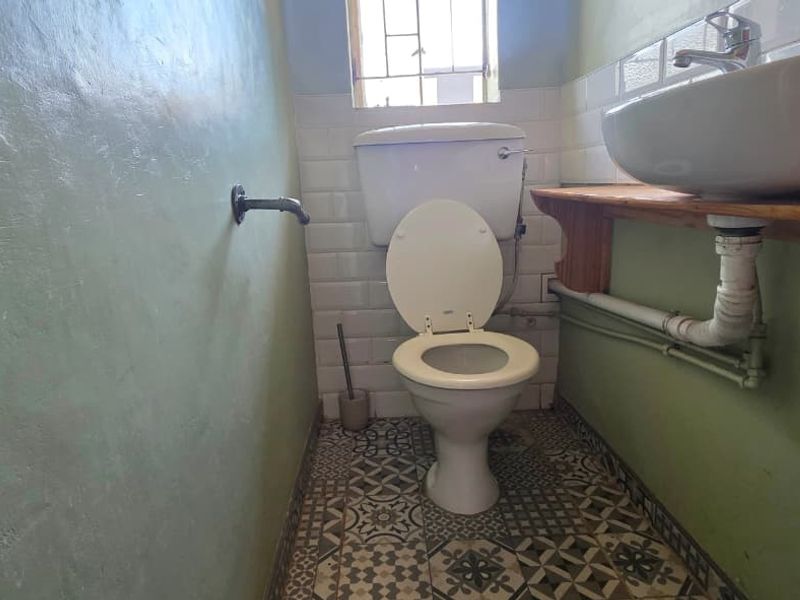A compact bathroom featuring a toilet, wall-mounted washbasin, subway tile backsplash, and patterned floor tiles, requiring some cosmetic updates to the plumbing and vanity area.