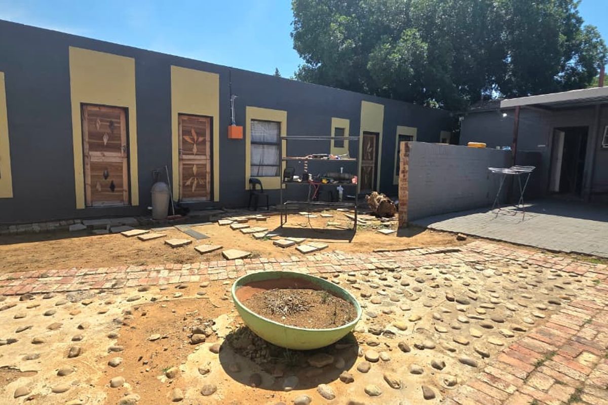 Rear exterior view featuring a paved patio area, multiple access doors, and a low-maintenance garden space with potential for landscaping improvements.