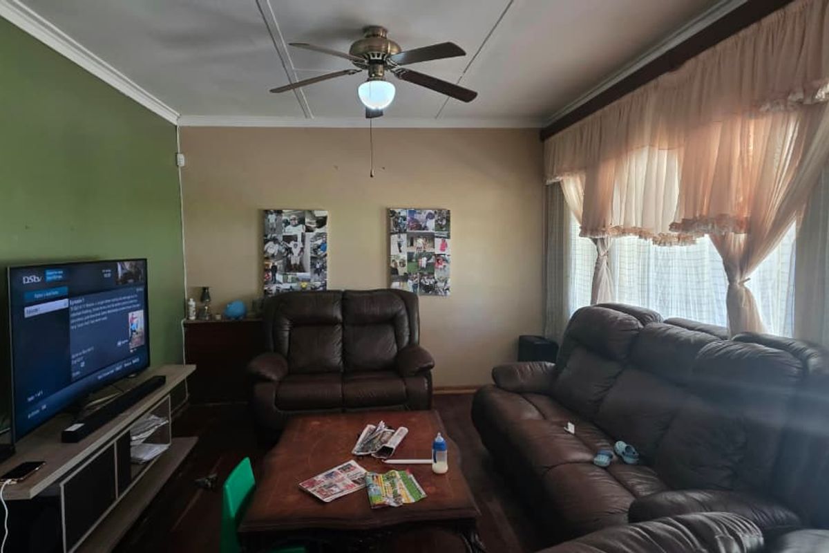 A comfortable living room featuring timber flooring, a ceiling fan, and large windows with natural light.