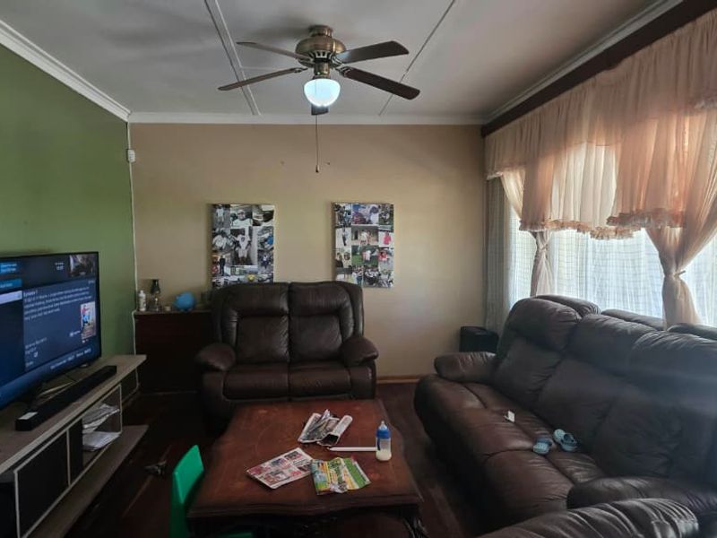 A comfortable living room featuring timber flooring, a ceiling fan, and large windows with natural light.