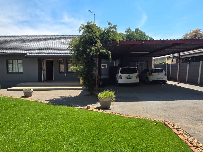 Front exterior view of the house featuring a paved driveway, a spacious carport, and a well-maintained lawn area.