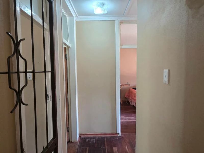 A narrow interior hallway featuring wooden flooring, a security gate, and access to adjacent rooms.