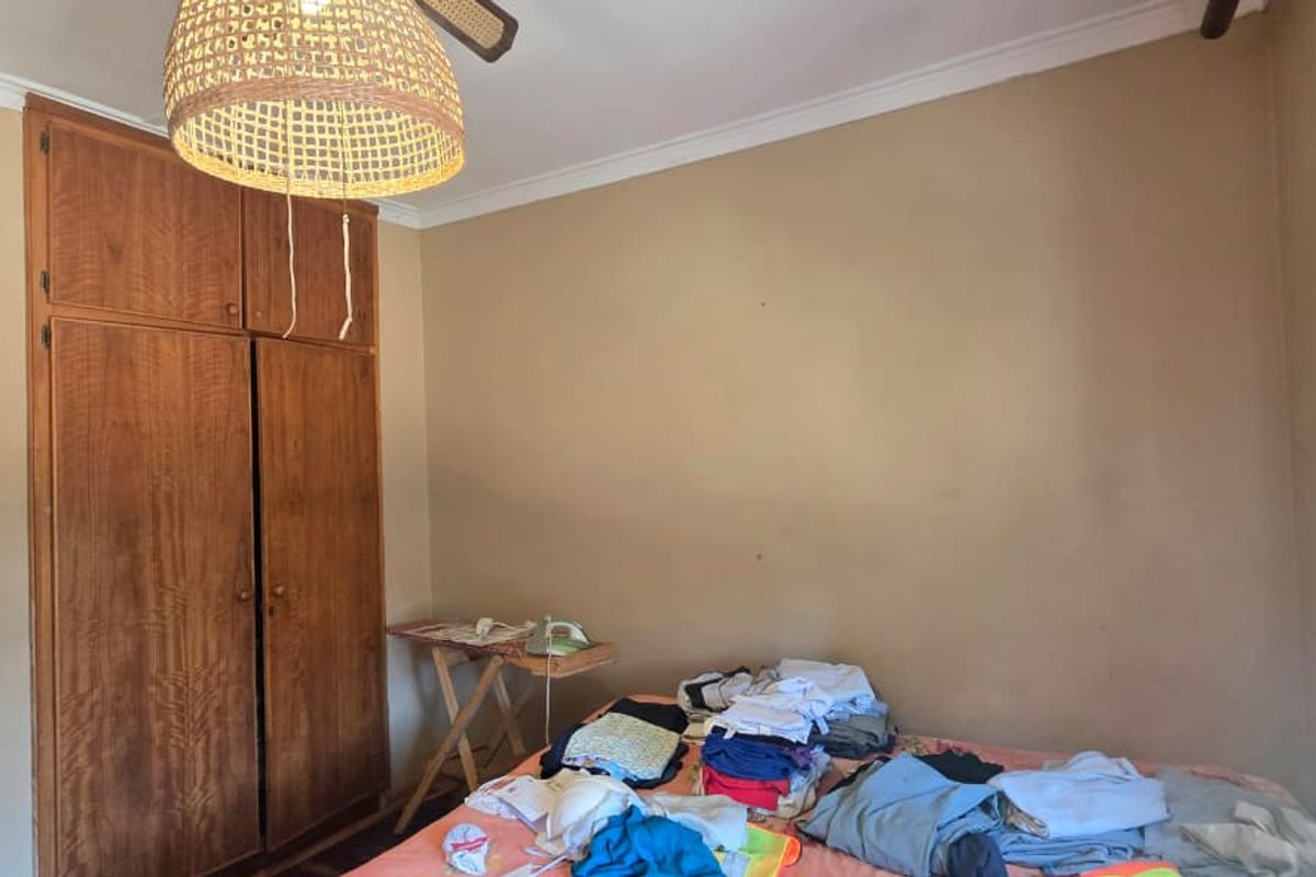 A bedroom featuring a built-in wooden wardrobe, ceiling fan, and cornice detailing, requiring cosmetic updates to the wall finishes.