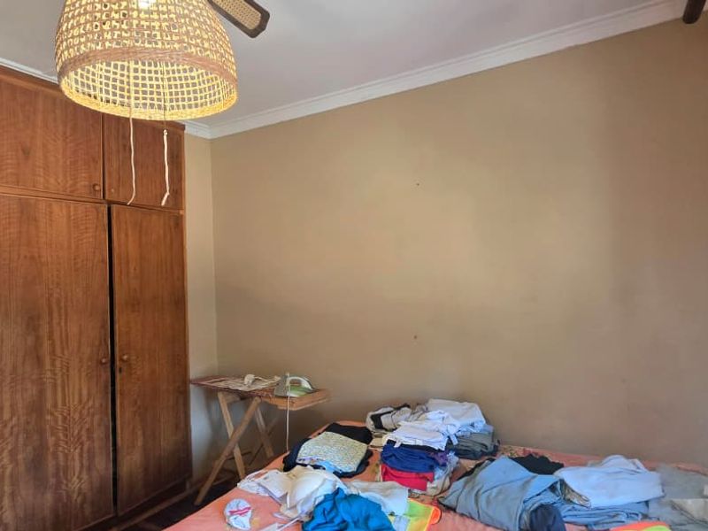 A bedroom featuring a built-in wooden wardrobe, ceiling fan, and cornice detailing, requiring cosmetic updates to the wall finishes.