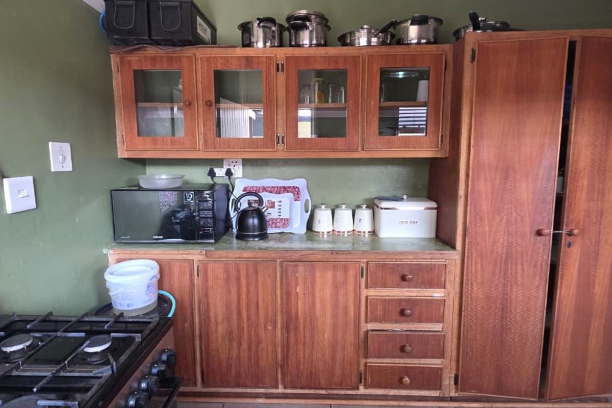 A functional kitchen featuring wooden cabinetry, a gas stove, and decorative tiled splashbacks, offering a dated aesthetic ready for modernization.
