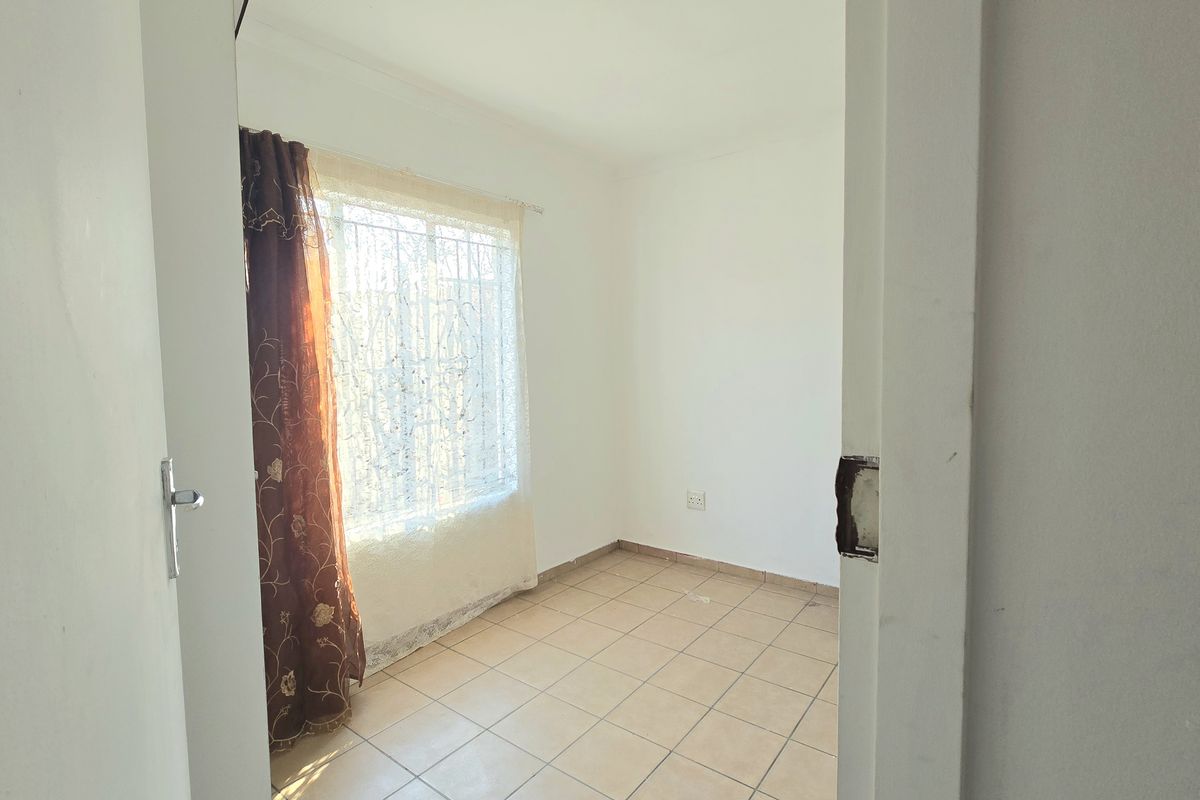 An empty bedroom featuring tiled flooring and a window fitted with security bars, requiring minor cosmetic updates.