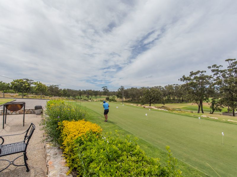 A scenic view overlooking a well-maintained golf course green, featuring a stone-edged patio area and landscaped garden borders.