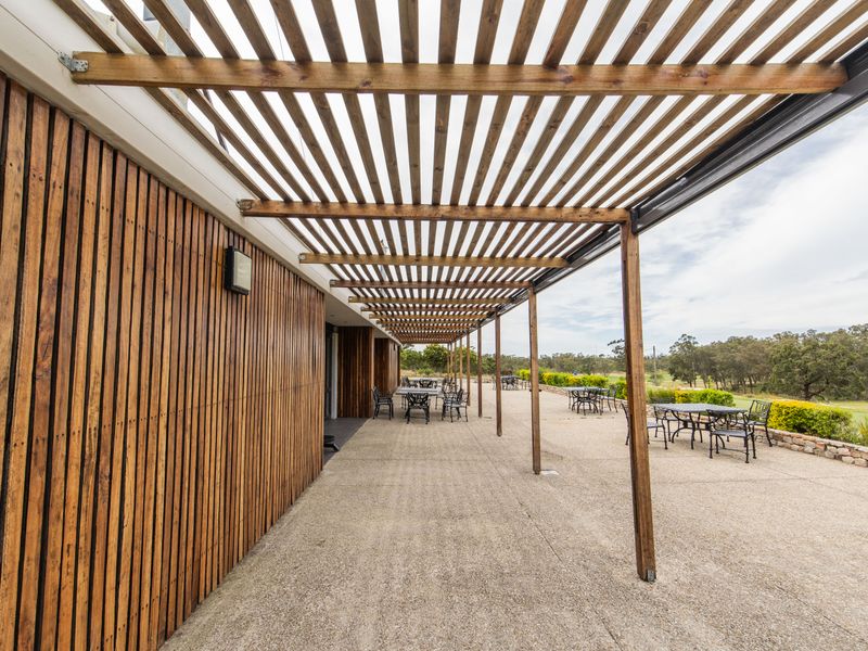 Spacious outdoor patio featuring a timber pergola, vertical timber slat wall cladding, and concrete flooring, overlooking a landscaped garden area.