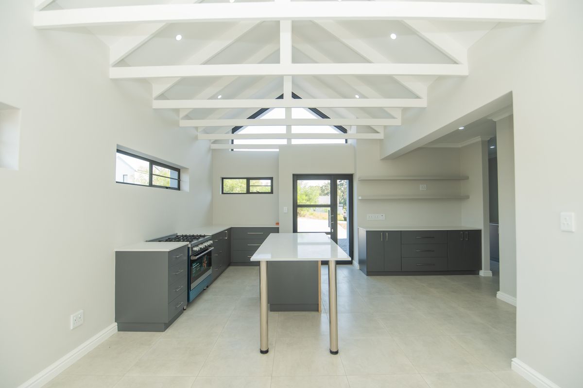Modern kitchen featuring a central island, dark grey cabinetry, gas stove, and high vaulted ceilings with exposed white trusses, creating a bright, open-plan space.