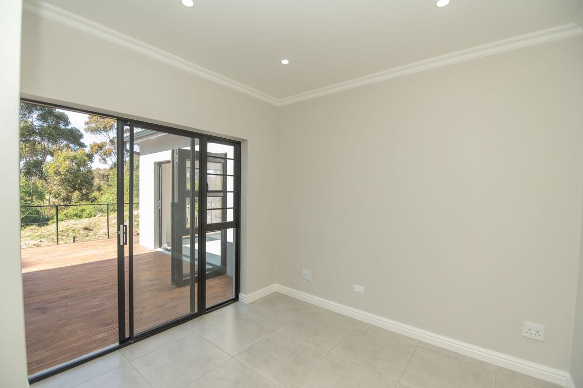 A bright, empty living room featuring neutral walls, crown molding, tiled flooring, and large sliding glass doors that open onto an outdoor wooden deck.