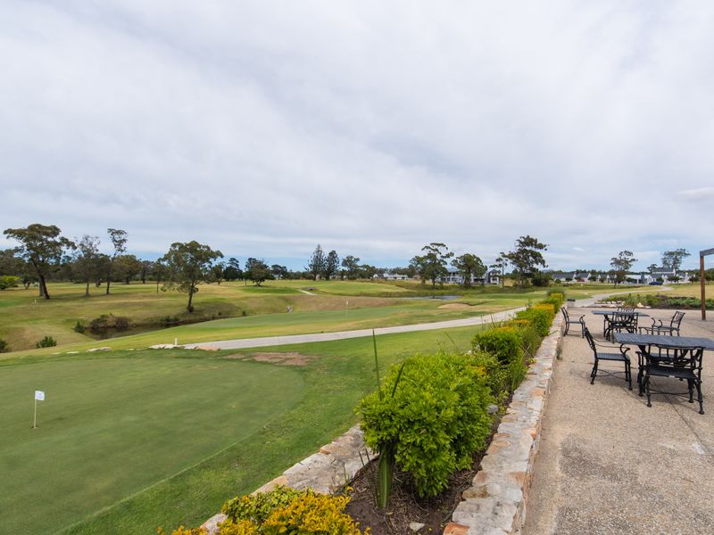 Scenic view overlooking a golf course with a stone retaining wall and paved patio area in the foreground.