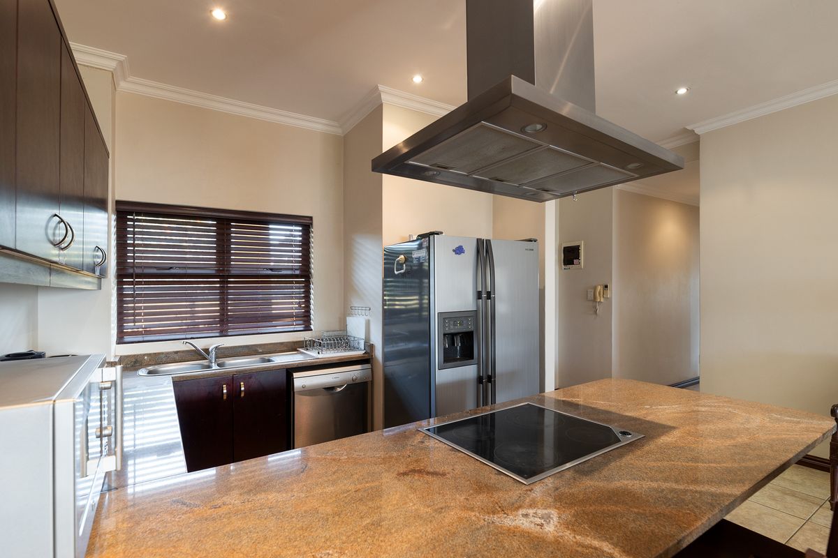 A well-appointed kitchen featuring granite countertops, a central island with an integrated electric hob, stainless steel extractor fan, and ample built-in cabinetry.