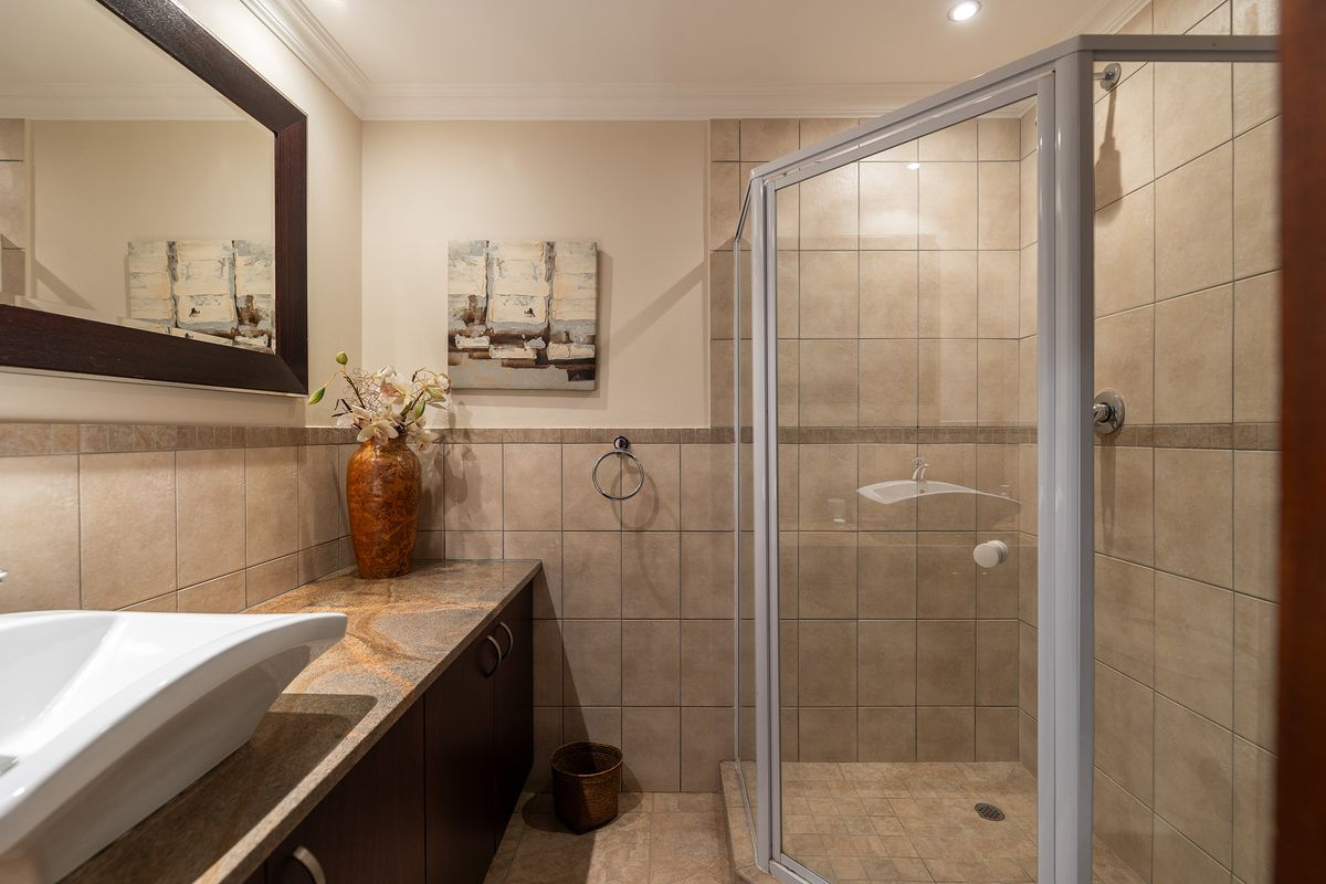 A well-maintained bathroom featuring a modern vessel sink on a stone countertop, dark cabinetry, and a corner shower enclosure with neutral wall tiling.