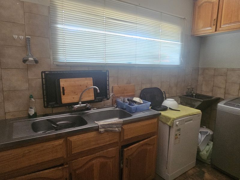A functional laundry area featuring wooden cabinetry, a double stainless steel sink, tiled splashbacks, and a secondary utility sink.