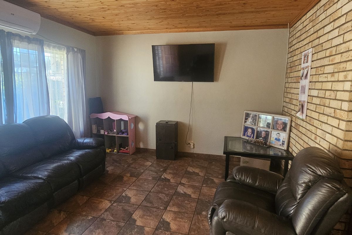A comfortable living room featuring a rustic exposed brick wall, warm timber ceiling, and durable tiled flooring, equipped with a wall-mounted air conditioning unit.