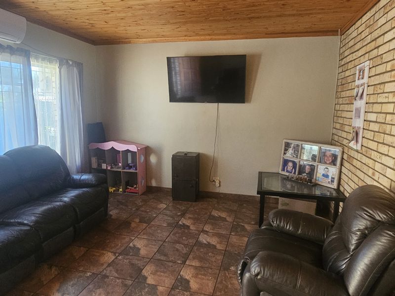 A comfortable living room featuring a rustic exposed brick wall, warm timber ceiling, and durable tiled flooring, equipped with a wall-mounted air conditioning unit.