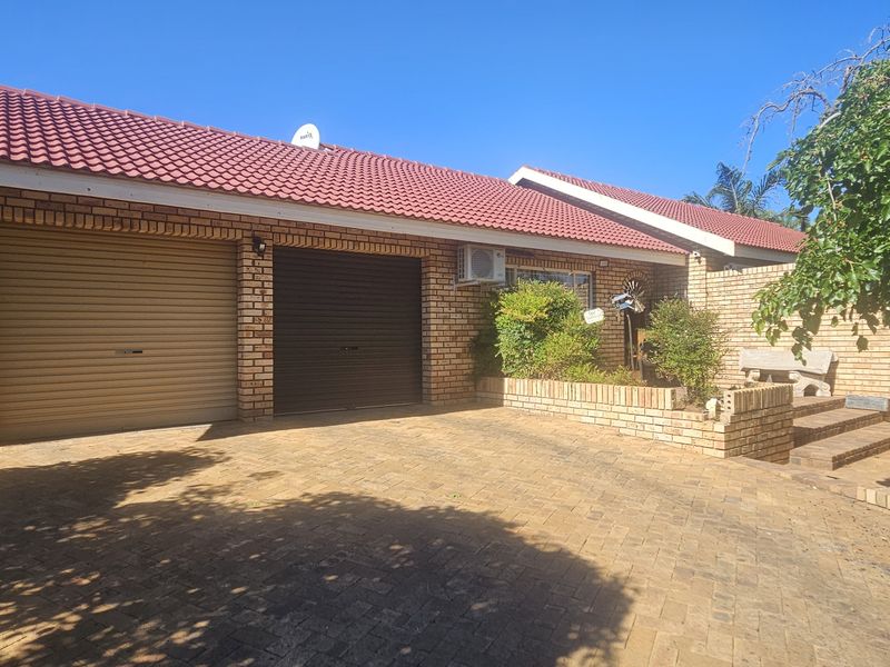 Front exterior view of a brick house featuring a double garage, paved driveway, and a tiled roof with an integrated air conditioning unit.