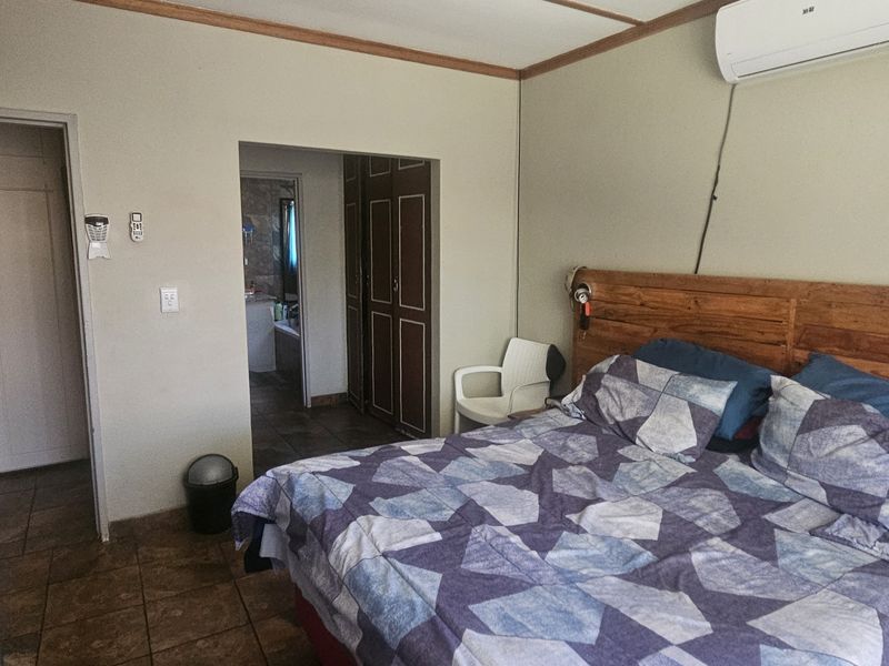A functional bedroom featuring tiled flooring, built-in cupboards, and a wall-mounted air conditioning unit, with an adjoining en-suite bathroom.