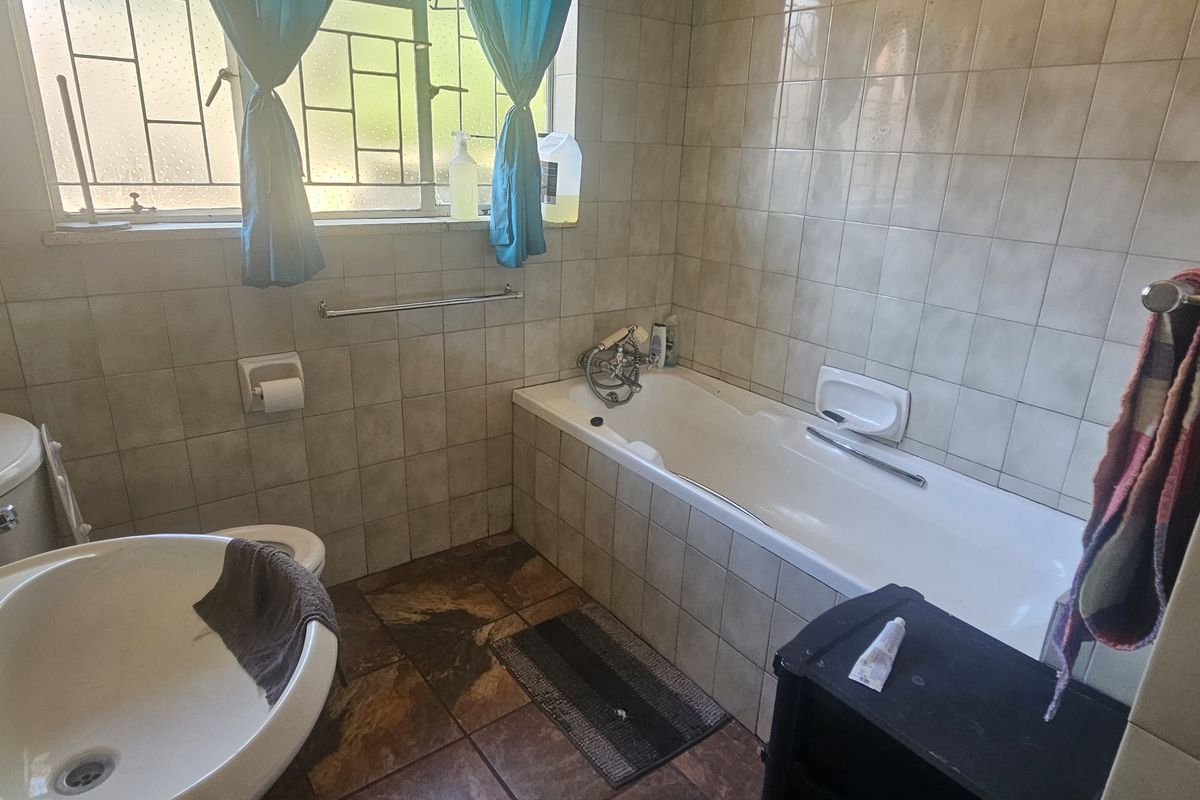 A functional bathroom featuring a bathtub, pedestal basin, and toilet, finished with neutral wall tiles and dark floor tiles.