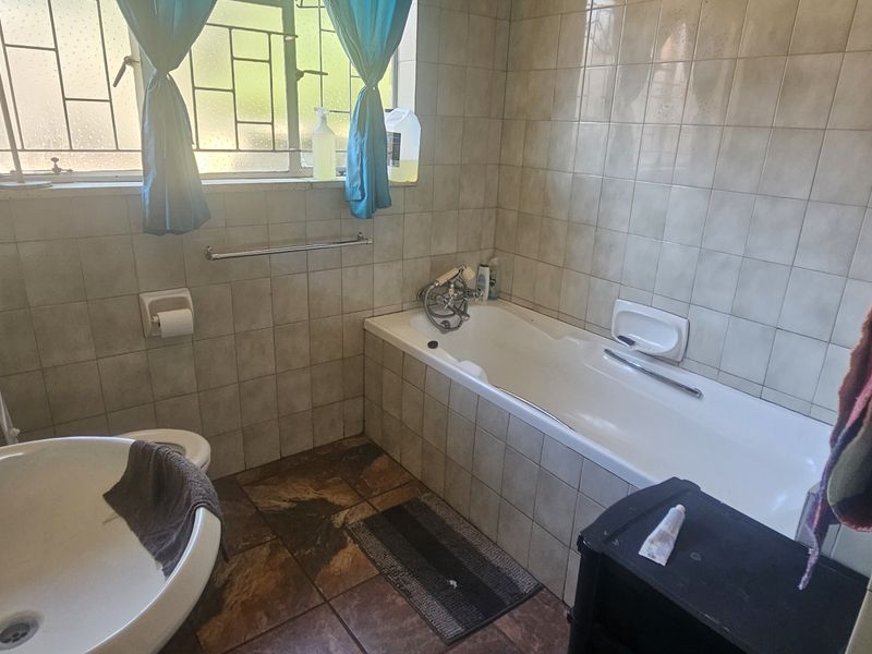 A functional bathroom featuring a bathtub, pedestal basin, and toilet, finished with neutral wall tiles and dark floor tiles.