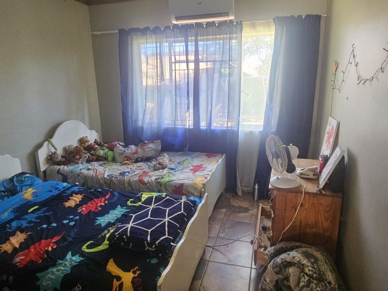 A functional bedroom featuring tiled flooring, a wall-mounted split-system air conditioner, and window security bars for added safety.