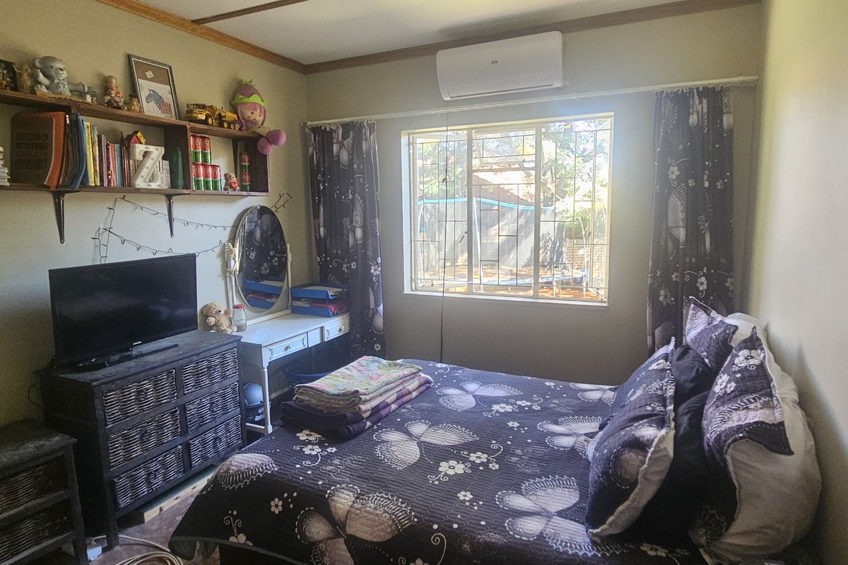 A functional bedroom featuring a wall-mounted air conditioning unit, security bars on the window, and built-in shelving.