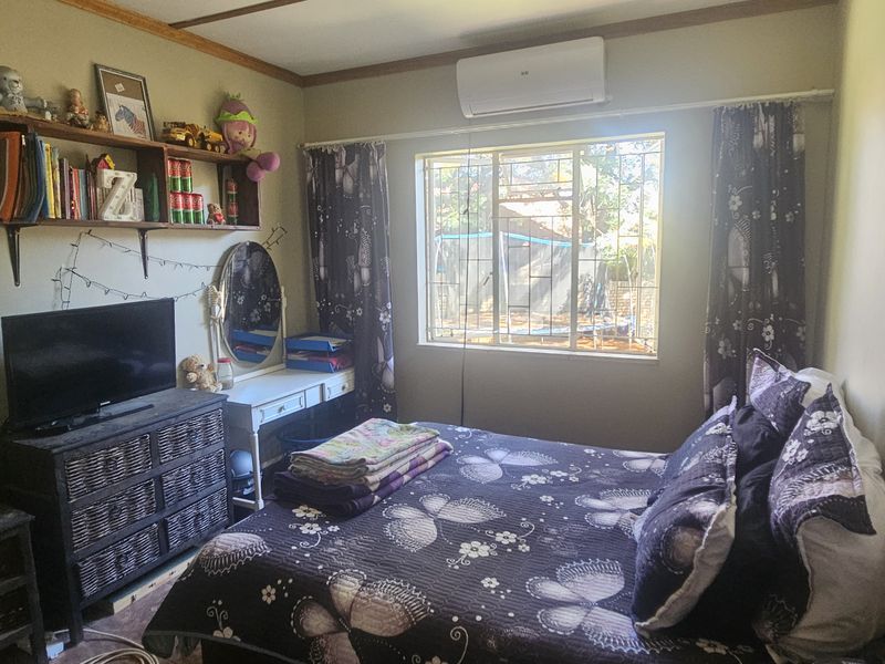 A functional bedroom featuring a wall-mounted air conditioning unit, security bars on the window, and built-in shelving.