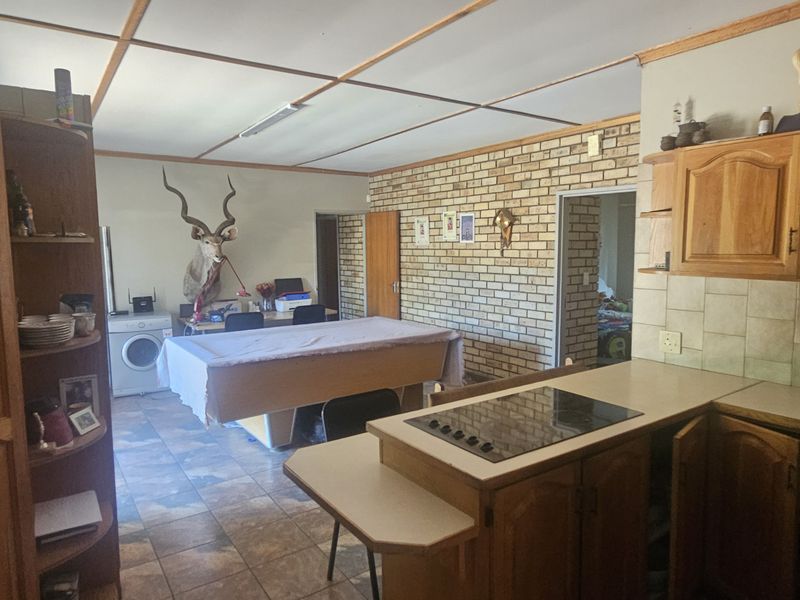 Open-plan kitchen and living area featuring wooden cabinetry, tiled flooring, and an exposed brick feature wall, offering a functional layout with potential for modernization.