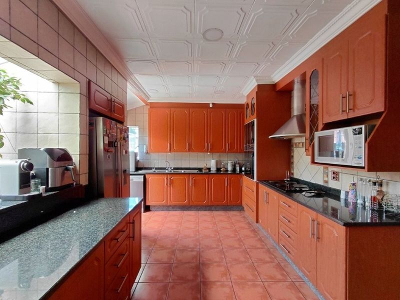 A spacious kitchen featuring extensive wooden cabinetry, granite countertops, a built-in microwave, stainless steel extractor fan, and decorative ceiling tiles.