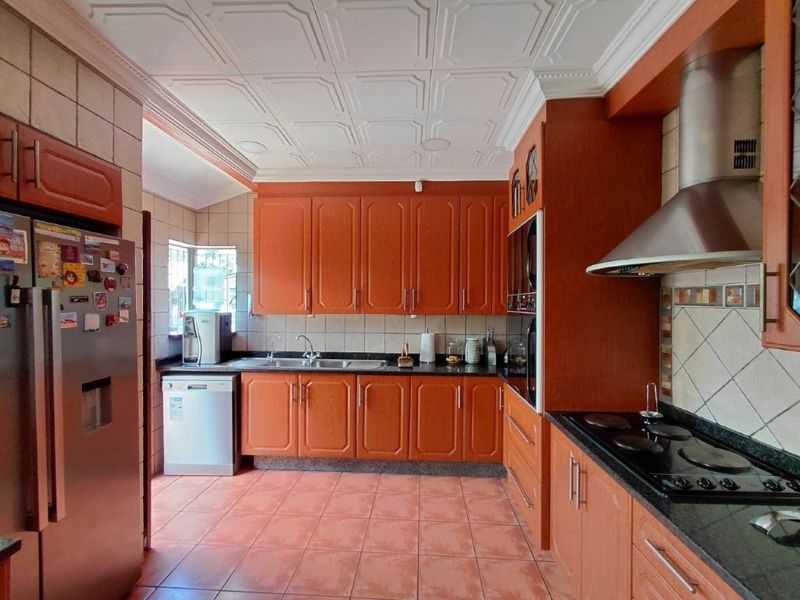 A functional kitchen featuring warm-toned cabinetry, granite countertops, built-in appliances, and decorative ceiling tiles, offering a classic layout with ample storage space.