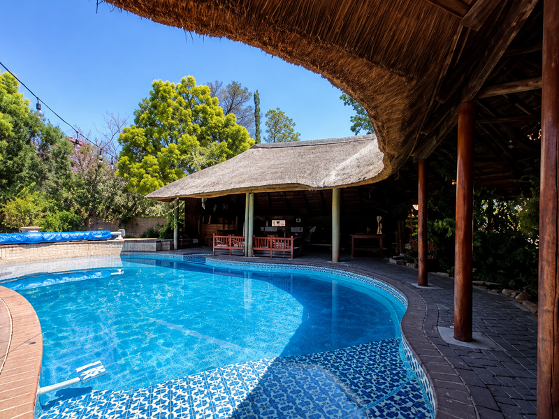 Outdoor pool area featuring a large swimming pool with decorative tiling, surrounded by a paved deck and a covered thatched entertainment space.