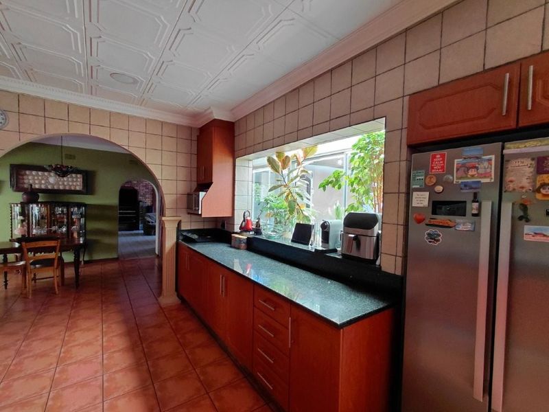 A functional kitchen featuring granite countertops, tiled splashbacks, and warm-toned cabinetry, connected to an adjacent dining area through a classic architectural archway.