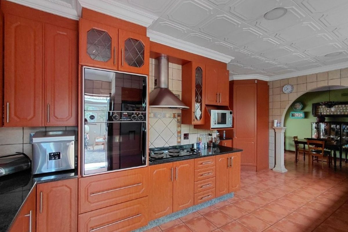 A traditional kitchen featuring warm-toned wooden cabinetry, built-in appliances, tiled flooring, and a decorative ceiling, with an open archway leading to the dining area.