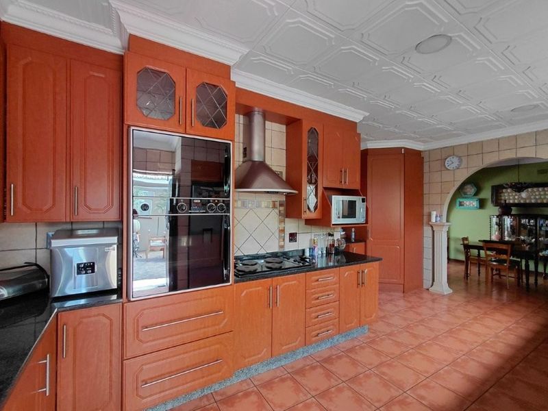 A traditional kitchen featuring warm-toned wooden cabinetry, built-in appliances, tiled flooring, and a decorative ceiling, with an open archway leading to the dining area.