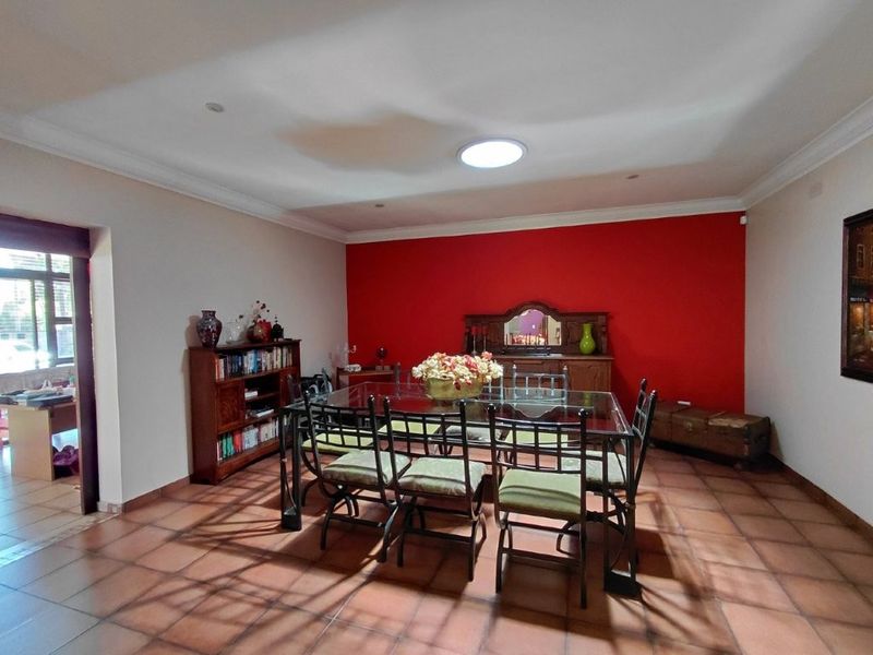 Spacious dining room featuring terracotta floor tiles, a prominent red accent wall, and a skylight providing natural illumination.