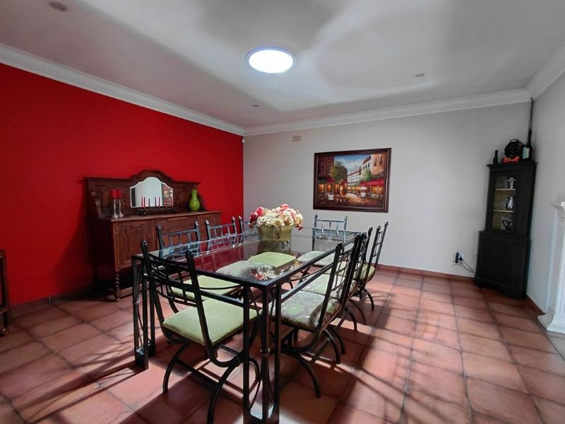 A spacious dining room featuring terracotta floor tiles, a skylight, and a bold red accent wall, providing a functional space for family meals.