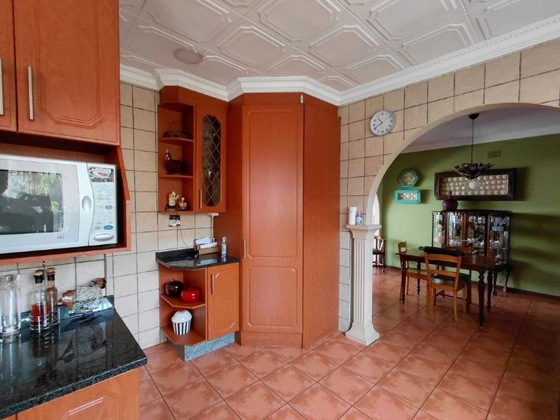 Open plan kitchen and dining area featuring wooden cabinetry, granite countertops, tiled flooring, and a decorative ceiling, connected by a classic archway.