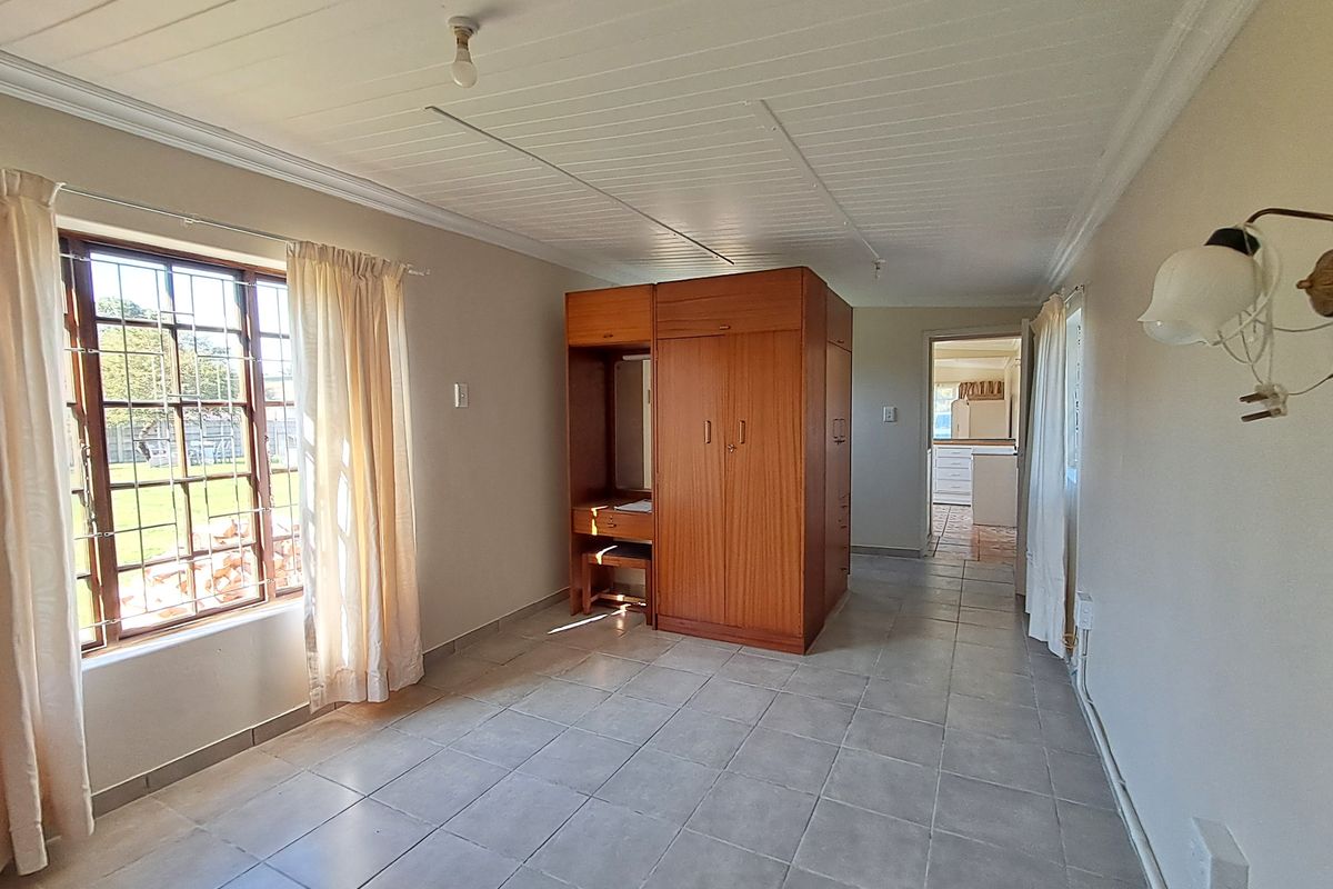 A bedroom featuring tiled flooring, a built-in wardrobe, and a tongue and groove ceiling, with security bars on the window.